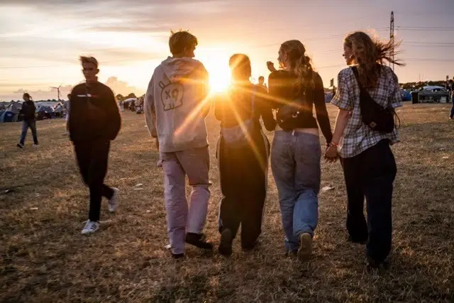 Fyra festivalbesökare som går bredvid varandra vid solnedgång på Roskildefestivalen