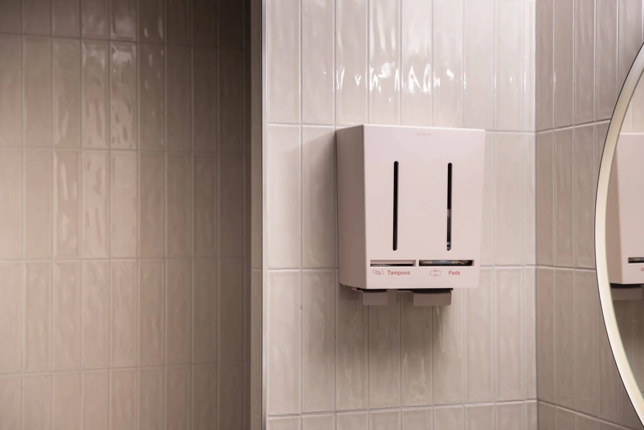 A picture in a restroom of a pink dispenser containing menstrual products.