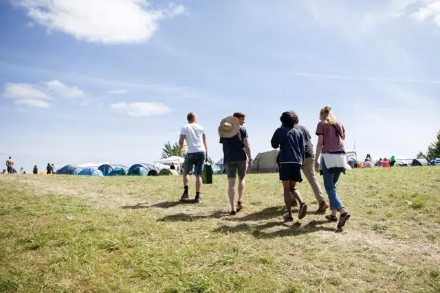Fem vänner på Roskildefestivalen en varm och solig sommardag, i bakgrunden syns flera festivaltält uppfällda