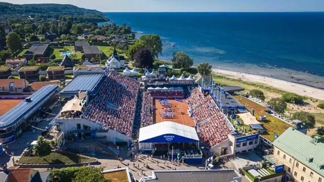 bild ovanifrån på tennisplan i Båstad med fullsatt publik, skogen till vänster och havet till höger