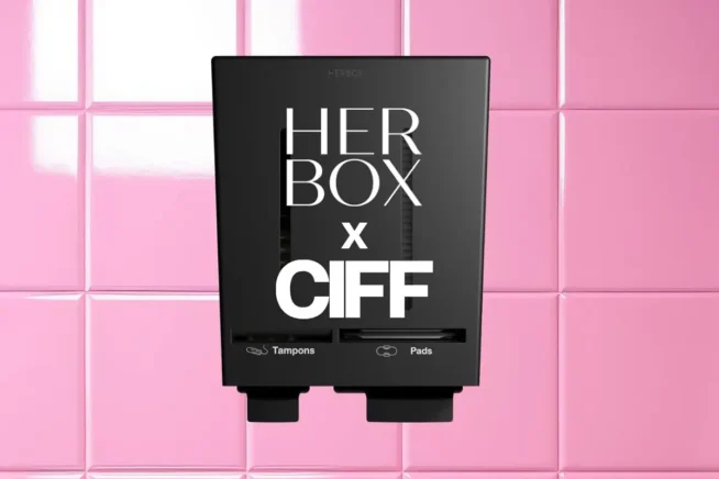 En bild på Herbox svarta combi dispenser med Herbox logotyp i vitt och CIFFs logotyp i vitt. Automaten sitter på en tuggummi-rosa vägg.